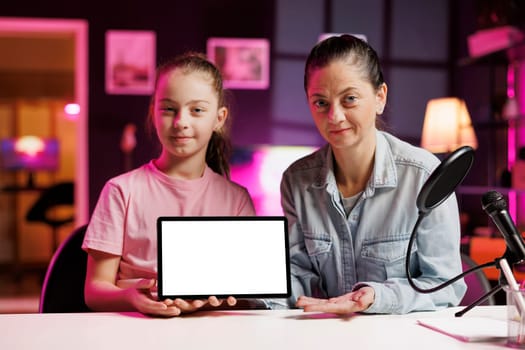 Cute girl and her mom filming unboxing mockup tablet popular among children watching her online content. Cheerful daughter and mother recording video unpacking isolated screen device