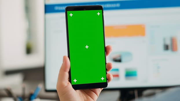 Company worker holding smartphone with greenscreen template, using digital chromakey template on mobile gadget display. Employee presenting isolated mockup copyspace in business office.