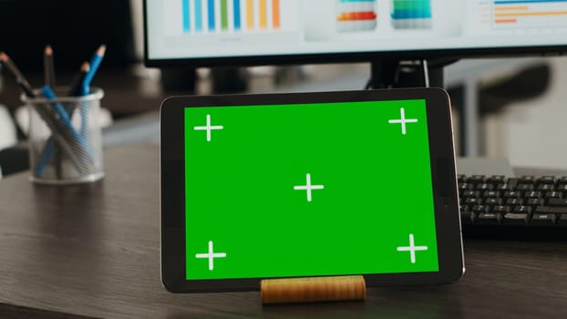 Digital tablet presenting greenscreen display on agency office desk, showing blank chromakey template at empty workstation. Modern mobile device displaying isolated chromakey concept. Close up.