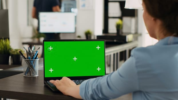 Business person using chromakey laptop with greenscreen template in startup office. Company employee looking at mockup copyspace with isolated mockup on wireless computer screen.