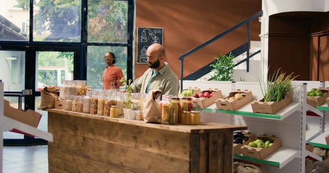 Client in sustainable market store looking at pasta or grains stored in reusable glass containers, local neighborhood zero waste shop. Buyer doing grocery shopping for organic chemicals free produce.