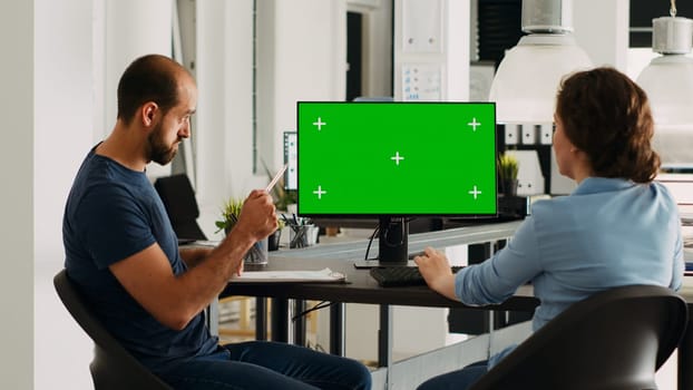 Corporate team using greenscreen on monitor while sitting at agency workstation, small business development. Man and woman colleagues looking at display showing isolated copyspace.