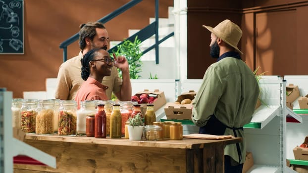 Couple asking local vendor about fresh produce in organic zero waste eco store, storekeeper recommending fruits and veggies freshly harvested from own garden. Seller presenting additives free food.