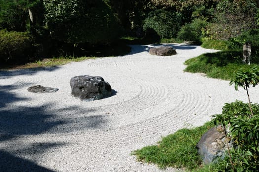 A serene Japanese Zen garden with raked white gravel, large rocks, and green foliage surrounding the area.