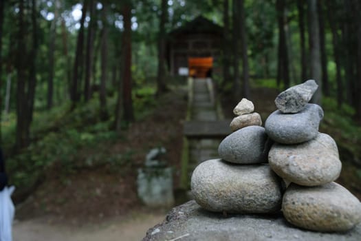 A small pile of balanced stones in the foreground with a forest and a shrine in the background.