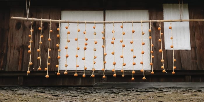 Rows of persimmons hanging on strings to dry outside a wooden building.