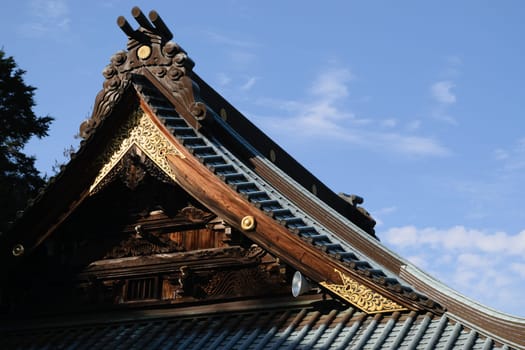 Close-up of a traditional Japanese temple roof with intricate wooden carvings and gold accents under a clear blue sky.