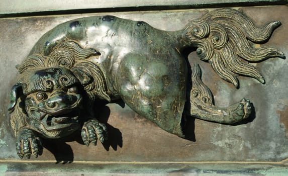 Close-up of a bronze sculpture depicting a mythical creature with a lion-like face and a flowing tail.