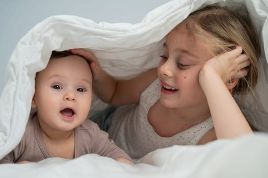 Little girl and her newborn brother hiding under the blanket