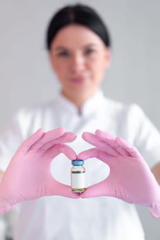 Blurred woman cosmetologist in pink gloves showing filler in vial in clinic. Young female dermatologist preparing for beauty treatment in hospital.