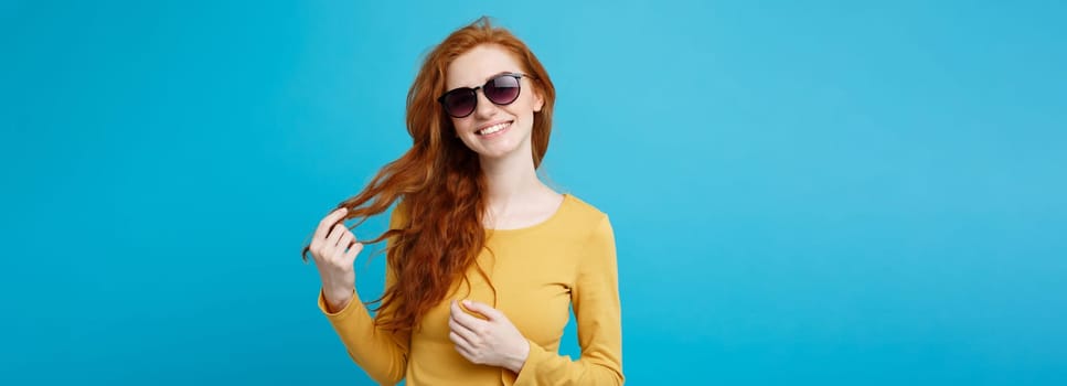 Travel concept - Close up Portrait young beautiful attractive ginger red hair girl with trendy sunglass smiling. Blue Pastel Background. Copy space