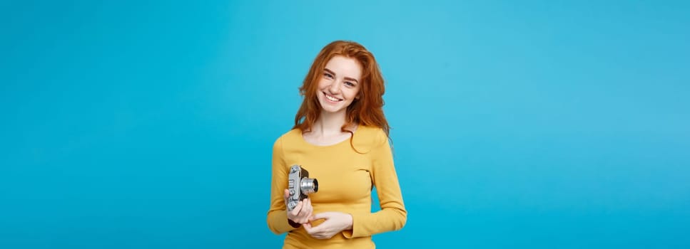 Close up Portrait young beautiful attractive ginger girl happy smiling with vintage camera and ready to travel. Isolated on Blue Pastel Background. Copy space