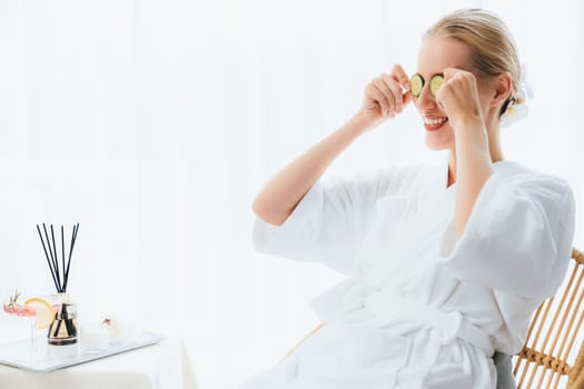 Woman holding slices of fresh cucumber and wearing bathrobe enjoying luxurious facial skincare spa in resort or hotel. Skin treatment for face and beauty care. Quiescent