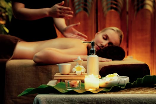 Aromatherapy massage ambiance or spa salon composition setup with focus decor candles and spa accessories on blurred woman enjoying blissful aroma spa massage in resort or hotel background. Quiescent