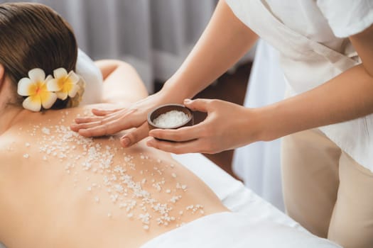 Woman customer having exfoliation treatment in luxury spa salon with warmth candle light ambient. Salt scrub beauty treatment in health spa body scrub. Quiescent