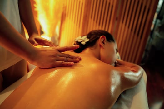 Closeup woman customer enjoying relaxing anti-stress spa massage and pampering with beauty skin recreation leisure in warm candle lighting ambient salon spa at luxury resort or hotel. Quiescent