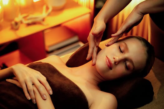 Caucasian woman enjoying relaxing anti-stress head massage and pampering facial beauty skin recreation leisure in warm candle lighting ambient salon spa in luxury resort or hotel. Quiescent