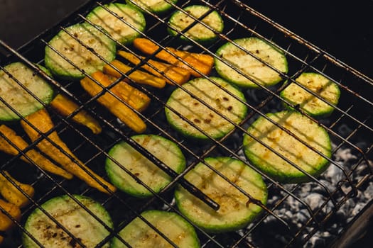Chopped zucchini and carrots roasting on fire seasoned with aroma herbs and spices. Delicious fresh vegetables grilling on barbecue smoker grid. Diet vegan bbq. Outdoor recreation in backyard