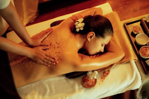 Woman customer having exfoliation treatment in luxury spa salon with warmth candle light ambient. Salt scrub beauty treatment in Health spa body scrub. Quiescent