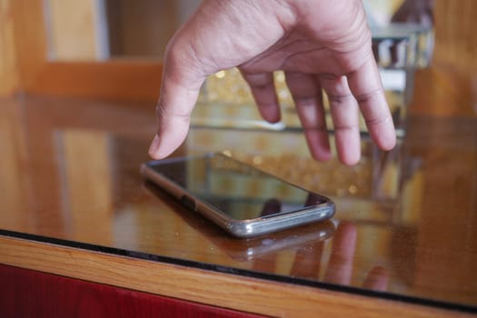 man hand picking up smart phone mobile from a table