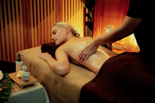 Caucasian woman customer enjoying relaxing anti-stress spa massage and pampering with beauty skin recreation leisure in warm candle lighting ambient salon spa at luxury resort or hotel. Quiescent