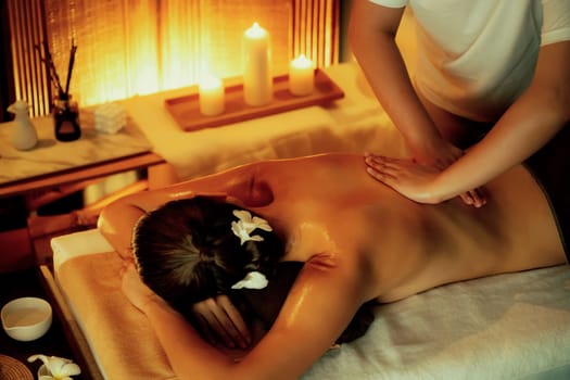 Caucasian woman customer enjoying relaxing anti-stress spa massage and pampering with beauty skin recreation leisure in warm candle lighting ambient salon spa at luxury resort or hotel. Quiescent