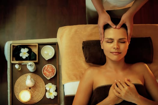 Caucasian woman enjoying relaxing anti-stress head massage and pampering facial beauty skin recreation leisure in warm candle lighting ambient salon spa in luxury resort or hotel. Quiescent