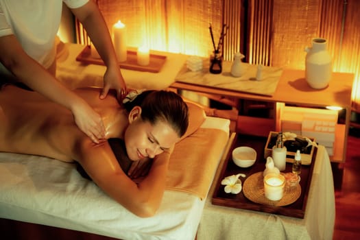 Caucasian woman customer enjoying relaxing anti-stress spa massage and pampering with beauty skin recreation leisure in warm candle lighting ambient salon spa at luxury resort or hotel. Quiescent