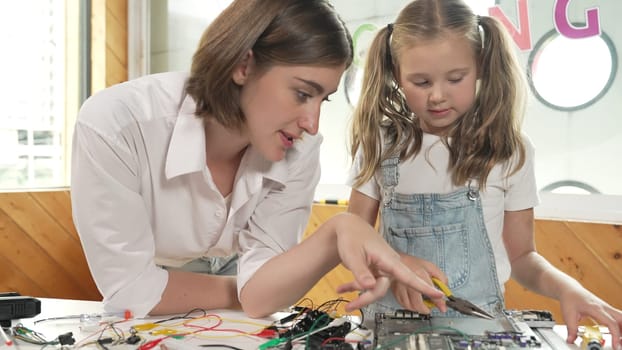 Young smart caucasian teacher teaching students about part of electronic board. Expert girl learn about digital electrical tool and fixing motherboard at table with chips and wires placed. Erudition.