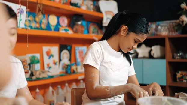 Caucasian highschool girl modeling cup of clay while diverse children laughing in art class at workshop. Multicultural student playing or making clay art in creative activity. Education. Edification.