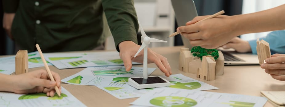 Windmill model represented renewable energy and wooden block represented eco city was placed on green business meeting table with environmental document scatter around. Front view. Delineation.