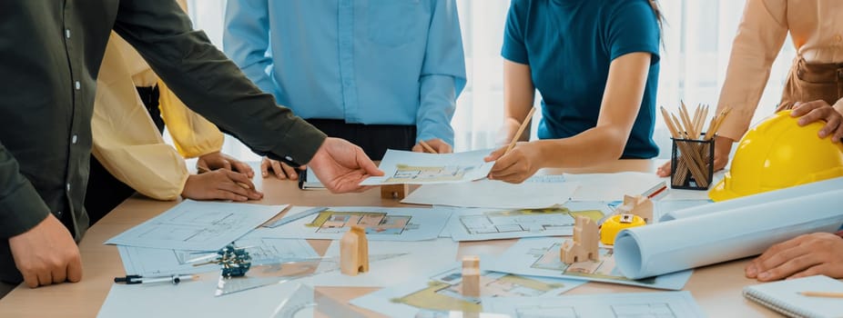 Professional architect engineer team discussion about architectural project on meeting table with wooden block and blueprint scatter around. Design and cooperate concept. Closeup. Delineation.