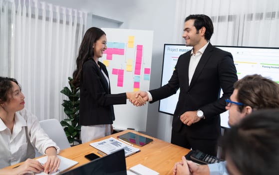 Cheerful meeting room, businesspeople celebrate with handshaking. Successful project was completed before the deadline. Business partnership and collaboration in project management. Habiliment