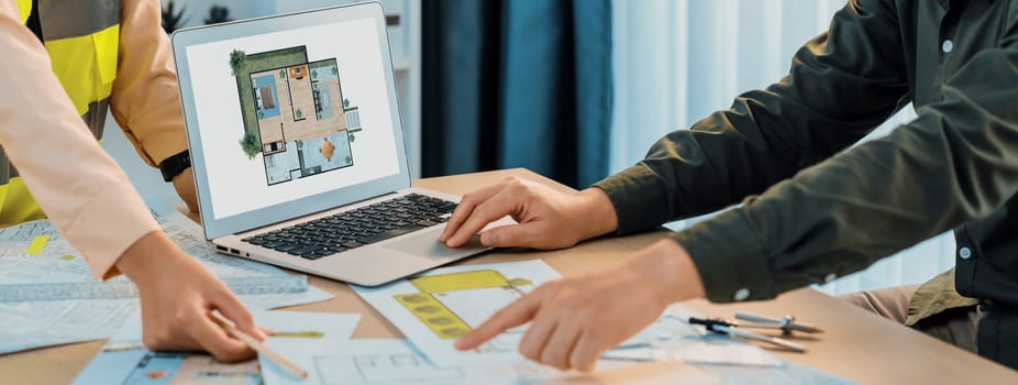 Professional architect shows mistake structure in blueprint while analysis and comparison with picture in laptop on table with blueprint and architectural equipment. Cropped image. Delineation.