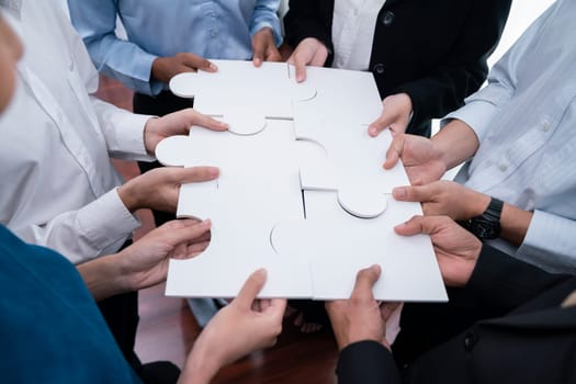 Diverse corporate officer workers collaborate in office, connecting puzzle pieces to represent partnership and teamwork. Unity and synergy in business concept by merging jigsaw puzzle. Concord