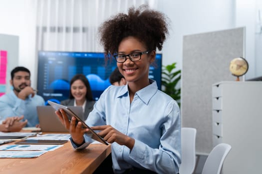 Happy young african businesswoman wearing glasses portrait with group of office worker on meeting with screen display business dashboard in background. Confident office lady at team meeting. Concord