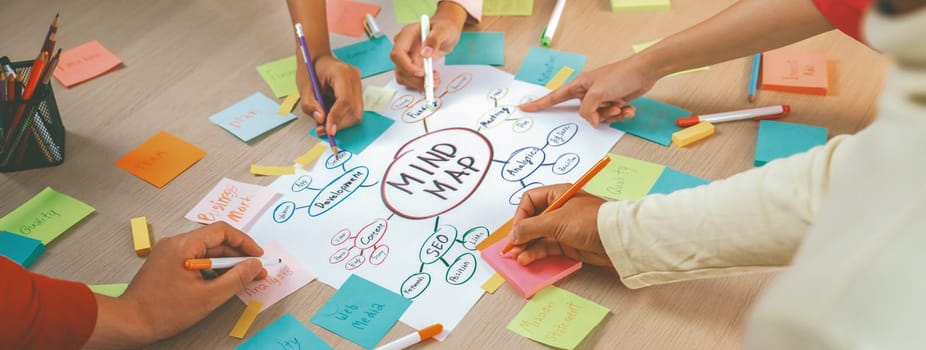 Professional startup group share creative marketing idea by using mind map. Young skilled business people brainstorm business plan while writing sticky notes. Focus on hand. Closeup. Variegated.