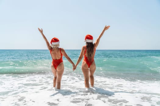 Women Santa hats ocean play. Seaside, beach daytime, enjoying beach fun. Two women in red swimsuits and Santa hats are enjoying themselves in the ocean waves and raising their hands up