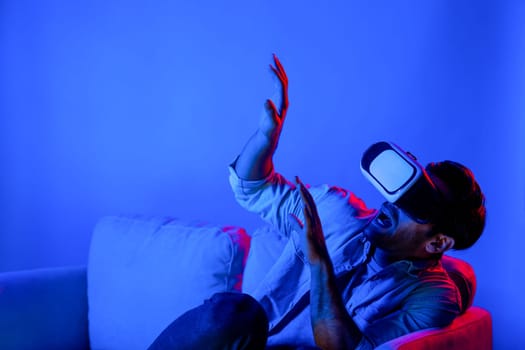 Scared person watching at horror movie by using VR goggles while sitting at sofa. Caucasian man looking at scary video or playing horror games by using virtual reality simulated world. Deviation.