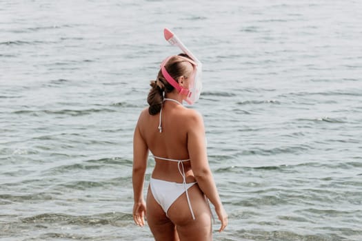 Young happy woman in white bikini put pink snorkeling mask on beach before swimming. girl having fun relaxing on beautiful beach. Beach lifestyle