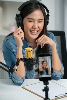 Host channel Asian influencer talking in broadcast wearing headsets on social media live on smartphone recording online, greeting listeners with coaching life or business at modern studio. Stratagem.