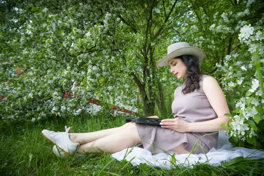 Girl engages with laptop amidst lush greenery. Freelancer Woman Working on Laptop Outdoors in a Blooming Garden