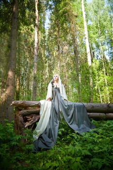 Adult mature woman 40-60 in a green long fairy dress in forest. Photo shoot in style of dryad and queen of nature. Fairy in beautiful green summer forest. Concept of caring for nature