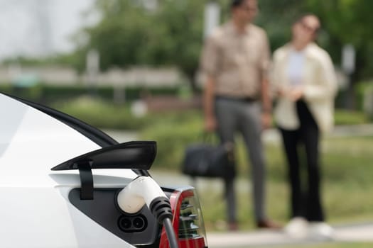 Young couple recharge electric car's battery from charging station in outdoor green city park in springtime. Rechargeable EV car for sustainable environmental friendly urban travel lifestyle.Expedient