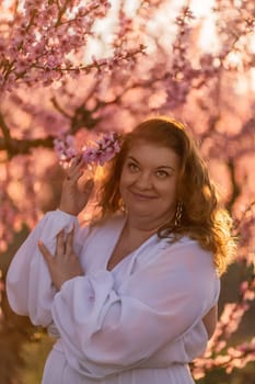 Woman blooming peach orchard. Against the backdrop of a picturesque peach orchard, a woman in a long white dress enjoys a peaceful walk in the park, surrounded by the beauty of nature