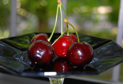 There is a red cherry on a black saucer.