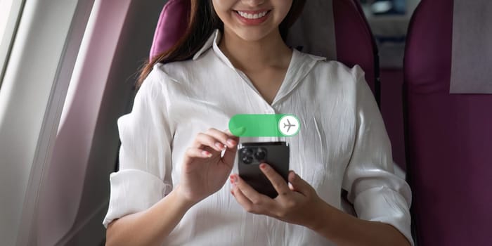 Asian business woman on airplane and turn on flight mode in her smartphone.