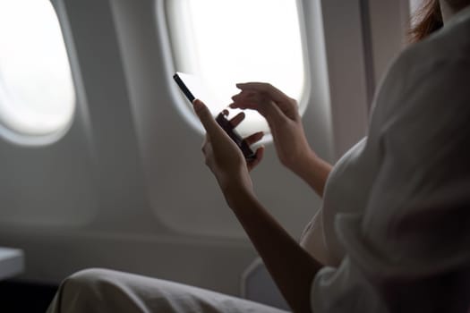 Asian business woman on aeroplane using smartphone.