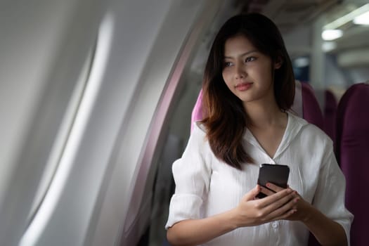 Asian business woman on aeroplane using smartphone.