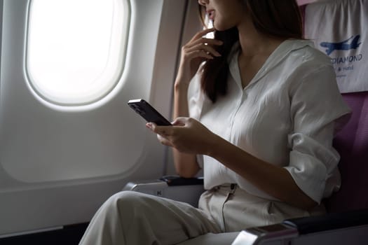 Asian business woman on aeroplane using smartphone.